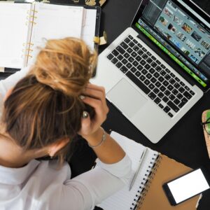 Overhead view of a stressed woman working at a desk with a laptop, phone, and notebooks.