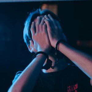 A person in handcuffs conceals their face under a blue light, suggesting a crime scene.