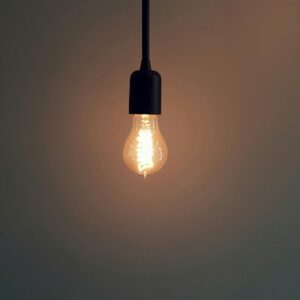 Simple illuminated light bulb hanging in a dark room, creating a warm atmosphere.