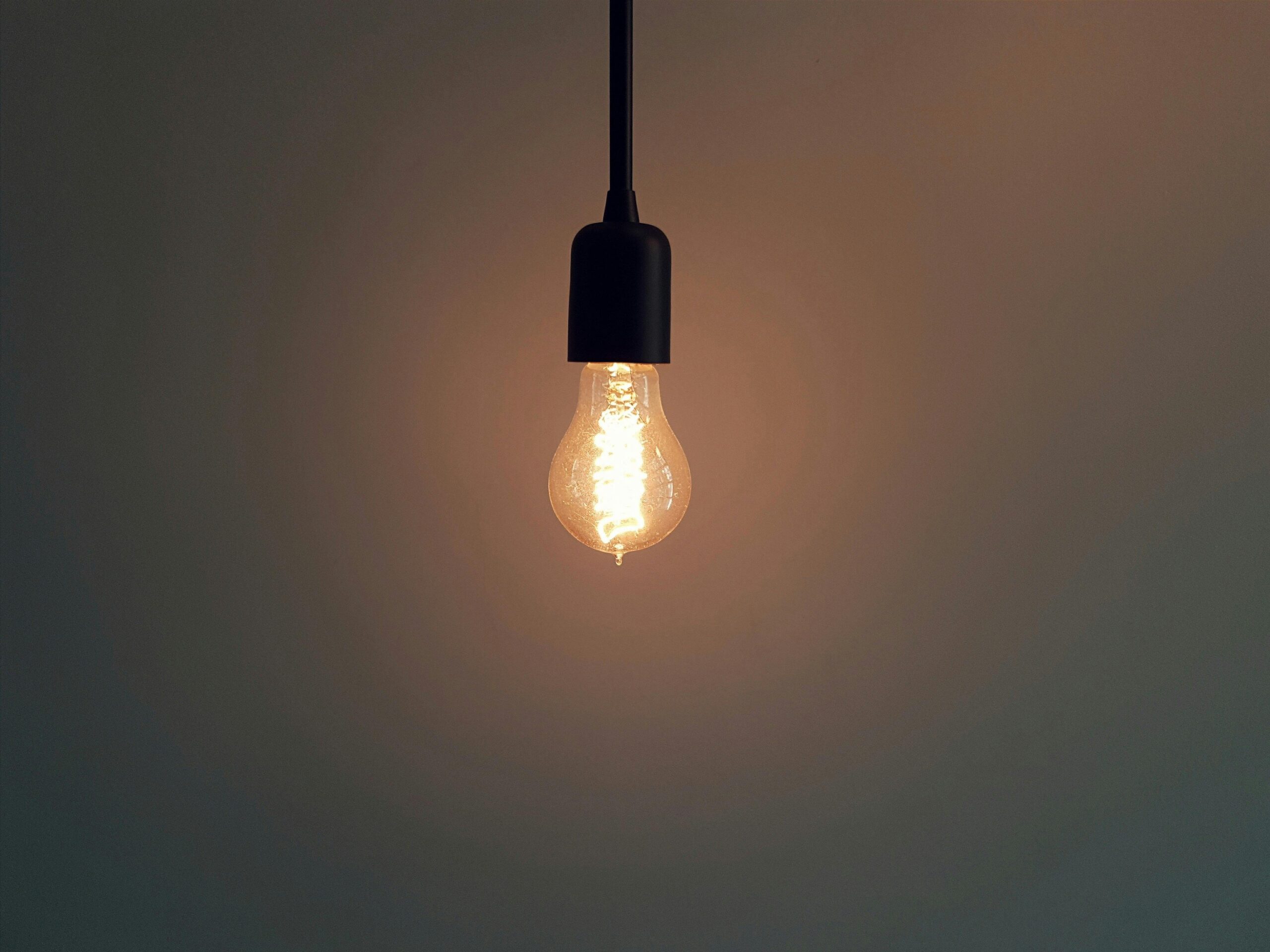 Simple illuminated light bulb hanging in a dark room, creating a warm atmosphere.